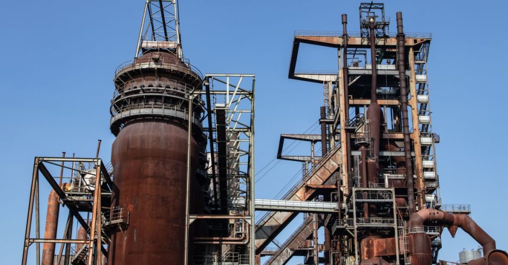 Close-up of a large rusted industrial metal structure with blue sky background.