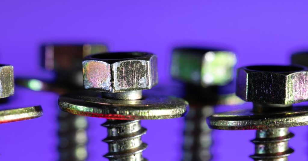 Detailed macro shot of metallic screws and bolts against a striking purple backdrop.