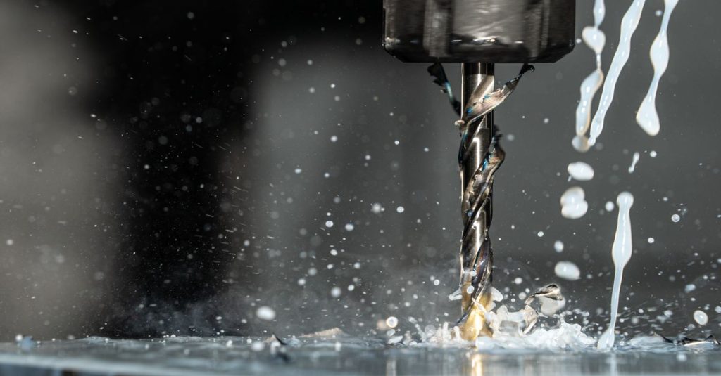 High-speed close-up of CNC drill bit in action with water splash for lubrication.