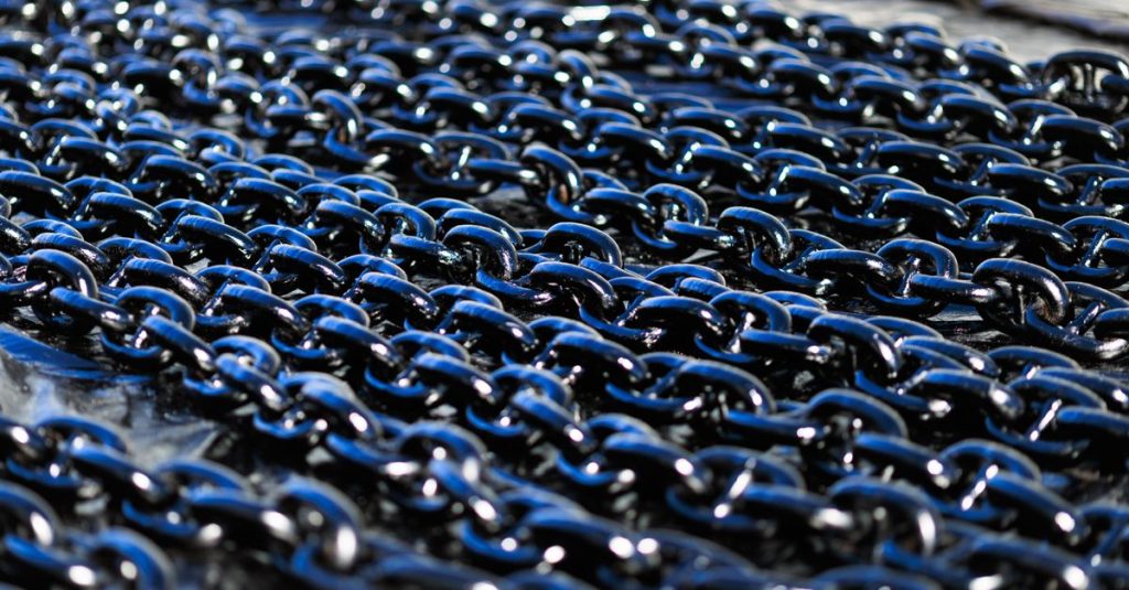 Detailed view of shiny industrial metal chains arranged outdoors, showcasing texture and metallic quality.