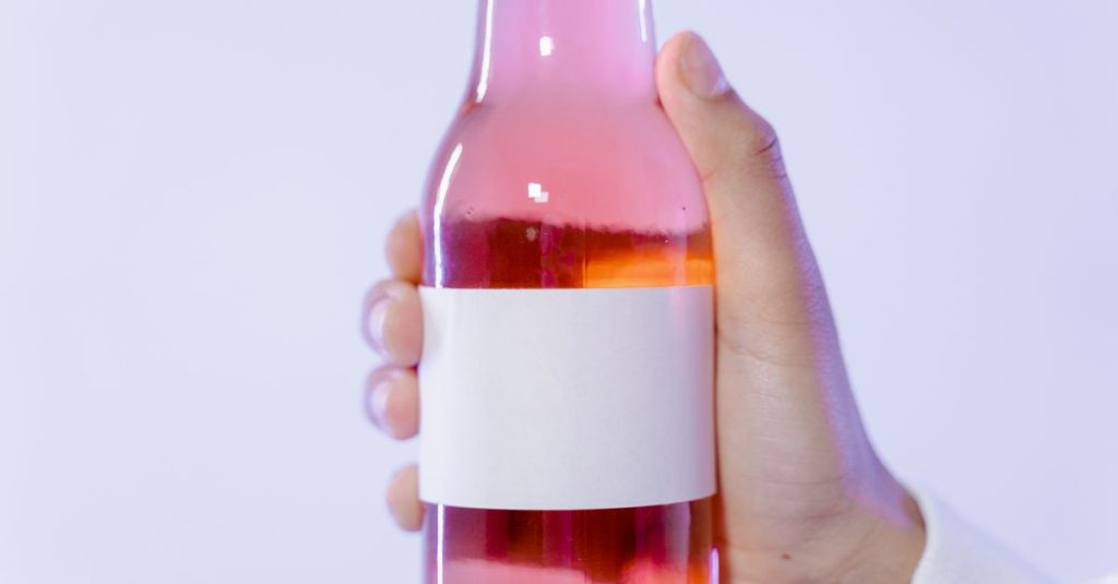 Close-up of a hand holding a pink glass bottle with a blank label for design.