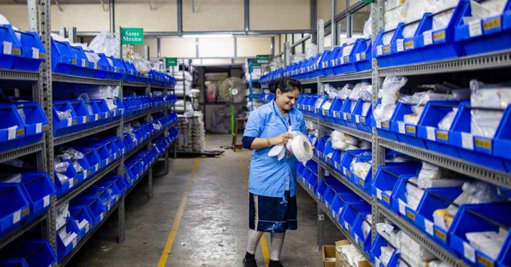A woman organizing inventory in a warehouse aisle, surrounded by shelves and blue bins.