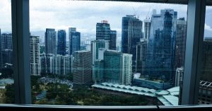 Overcast view of Kuala Lumpur's modern skyline through a rain-speckled window.