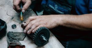 Detailed view of a technician working on a mechanical gear part with precision tools on a workbench.