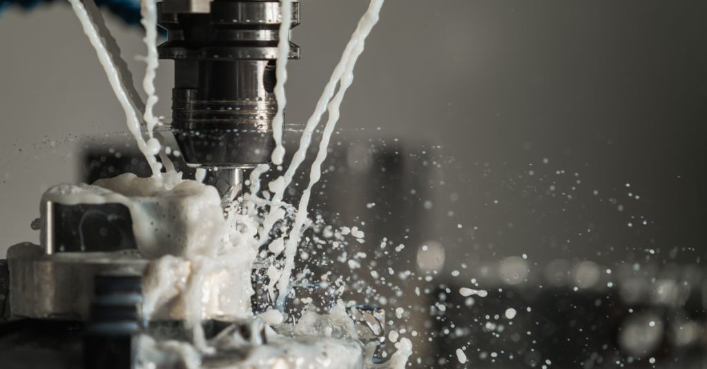Dynamic close-up of CNC machine with coolant splashing during metalwork operation.