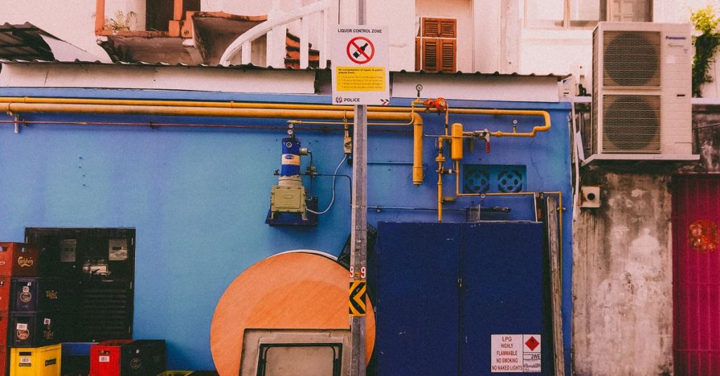 A vibrant urban alleyway featuring colorful utility boxes and pipes on a blue wall.
