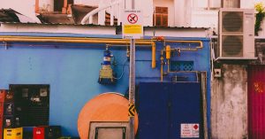 A vibrant urban alleyway featuring colorful utility boxes and pipes on a blue wall.