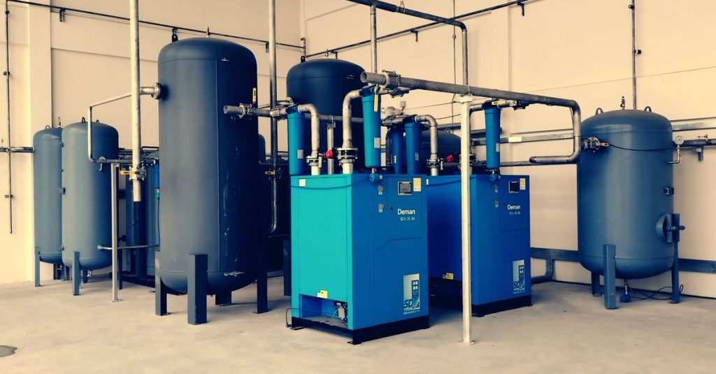 Industrial air compressor setup with blue tanks and pipes inside a plant.