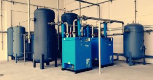 Industrial air compressor setup with blue tanks and pipes inside a plant.