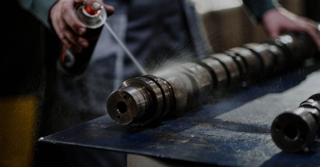 Mechanic meticulously sprays degreaser onto an engine camshaft for maintenance.