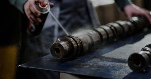 Mechanic meticulously sprays degreaser onto an engine camshaft for maintenance.