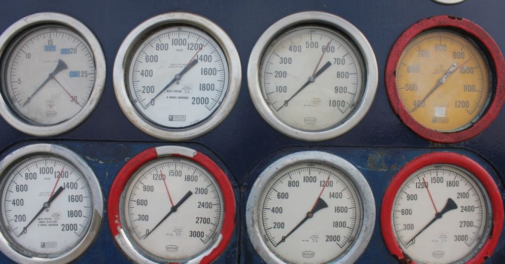 Close-up of multiple industrial pressure gauges on a blue metal panel, showing various readings.