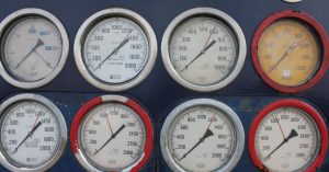 Close-up of multiple industrial pressure gauges on a blue metal panel, showing various readings.