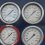 Close-up of multiple industrial pressure gauges on a blue metal panel, showing various readings.