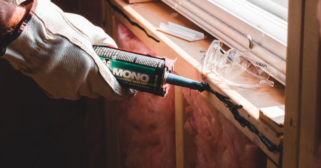 Crop unrecognizable workman in glove applying caulk from bottle on seam during window montage work in building