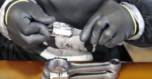 Close-up of a technician's hands assembling a metal connecting rod with precision and care.